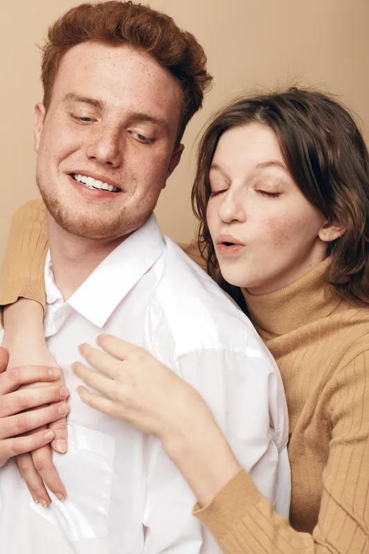 Young couple in casual clothes share a tender moment, woman embraces man from behind with eyes closed. Concept of love, affection, intimacy, and relationship happiness.