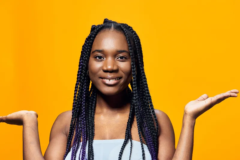 Cheerful black girl with long braided hair, showcasing positivity against a vibrant yellow background, perfect for concepts of happiness and self expression
