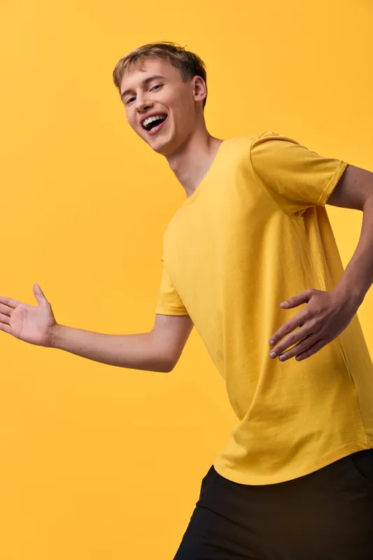Joyful man in a yellow shirt bursts with energy and smiles against a vibrant backdrop, capturing upbeat motion and positive mood.