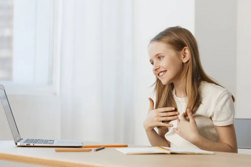Young girl interacting joyfully with a laptop at home, showcasing emotions of happiness and excitement in a bright, minimalistic environment