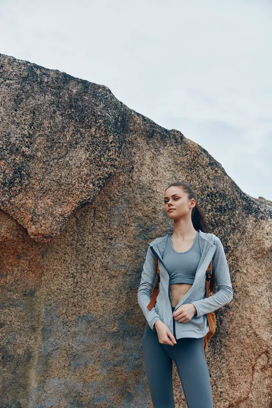 Athletic woman in stylish activewear posing confidently against a rocky background, representing fitness, health, and outdoor lifestyle