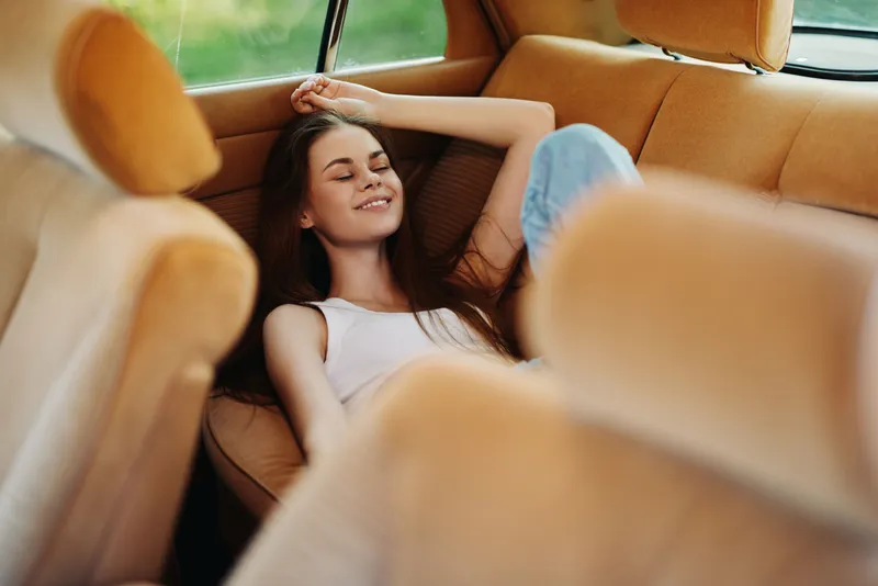Relaxed young woman enjoying a sunny day in a stylish vintage car interior, wearing casual clothing, exuding serenity and happiness.