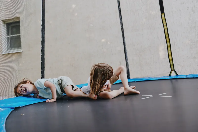 Two playful children having fun on a trampoline, expressing joy and creativity while enjoying their carefree summer day in an outdoor setting.