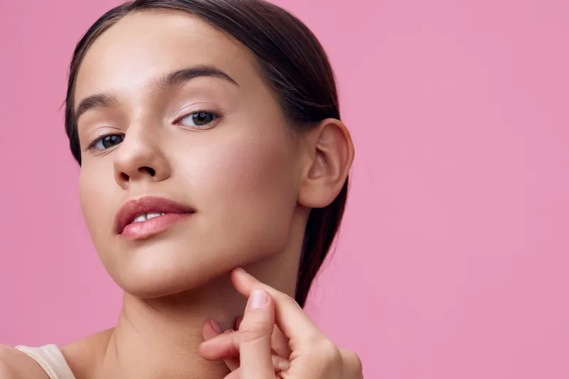 Young woman with flawless skin showing beauty routine against a pink background, emphasizing skincare and self care, ideal for wellness and beauty concepts