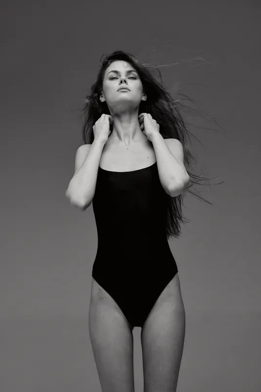Black and white portrait of a confident woman in a black swimsuit with natural hair and serene expression.
