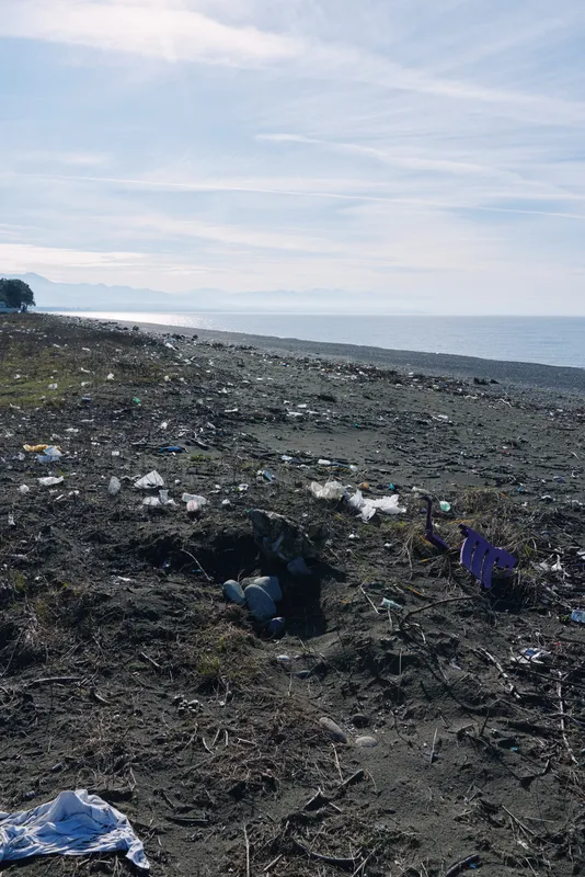 Rocky beach litter along the shoreline by a quiet sea, trash and debris scattered across the coast, polluted scenery calling for cleanup, conservation awareness, and responsible coastal care
