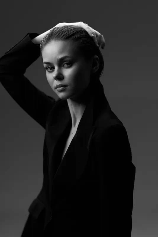 Black and white portrait of a contemplative woman with short hair wearing a dark blazer in a studio setting.