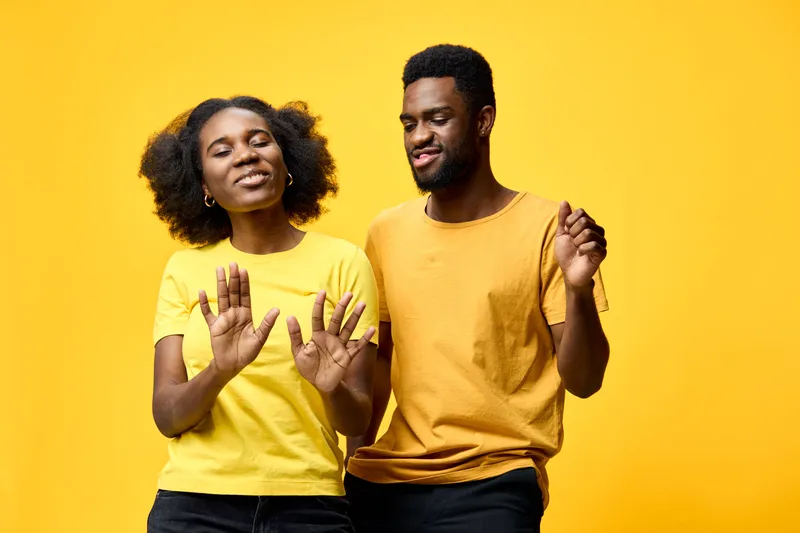 Happy African American couple dancing in bright yellow shirts on a vivid yellow background, conveying joy and connection