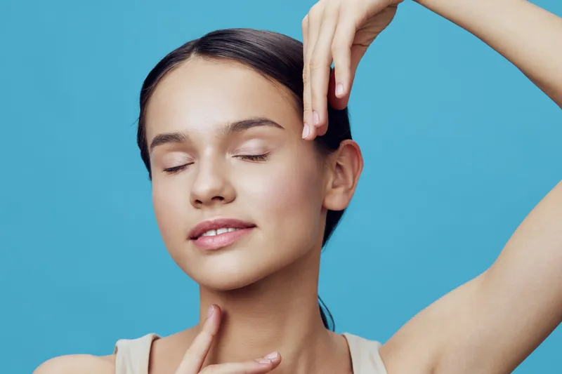 A serene young woman with closed eyes and a gentle smile poses against a light blue background, showcasing simple beauty and calmness in a skincare concept, emphasizing self care and well being