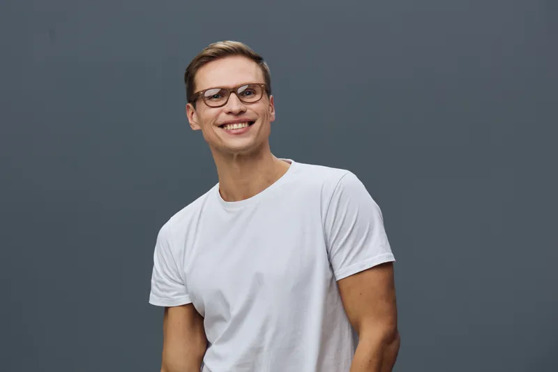 smiling young caucasian man wear glasses white t-shirt look camera isolated on dark gray background work from home digital nomad concept
