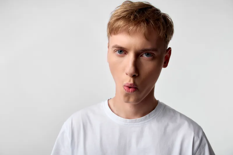 Young man, playful expression, kiss face, white t shirt, studio, neutral background, close up, facial expression, fashion, lifestyle, youth, cheerful, expressive, casual wear, modern vibe, clean