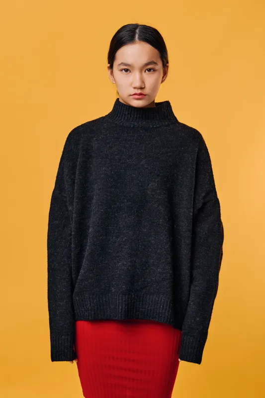 Young woman standing in dark oversized sweater and red skirt against yellow background. Portrait with serious expression, minimal style fashion and casual outfit for autumn or winter season.