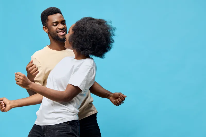 Joyful couple dancing together on a vibrant blue background, showcasing love and happiness through their expressions and colorful attire