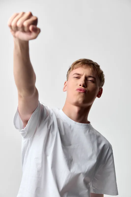 Victory gesture, young man raises fist in triumph, wearing a white shirt, bold pose, energetic mood, celebration of achievement, dynamic studio shot, confident stance, expressive motion and