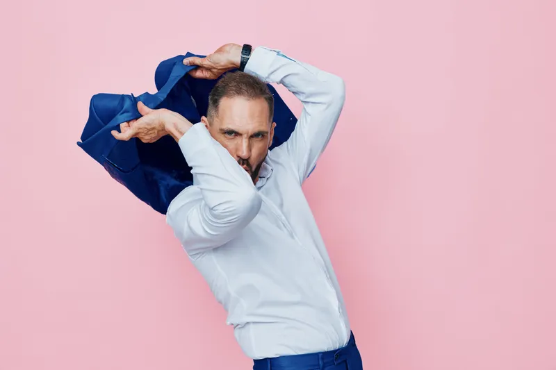 Professional businessman on a pink studio backdrop, posed with a dynamic gesture. Emotions of confidence and surprise convey determination and readiness for change in a bold, isolated color setting.