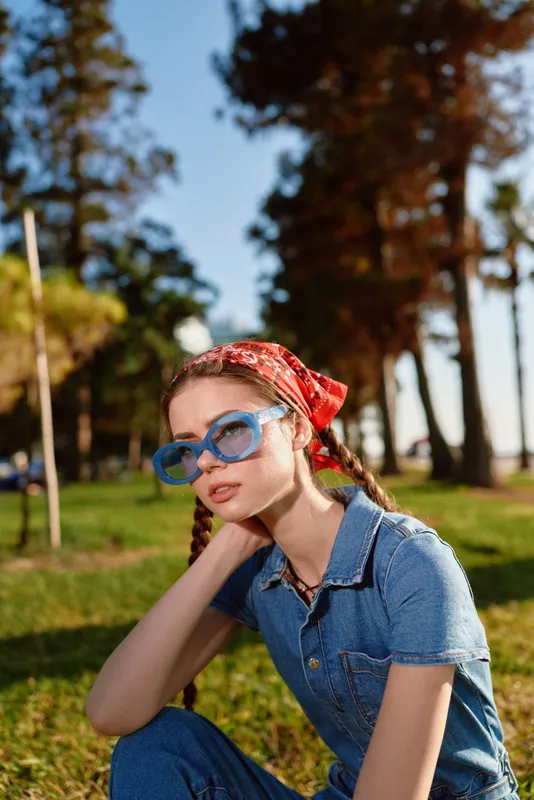 Lifestyle woman in modern boho-western denim street style poses outdoors with blue sunglasses and a red bandana, film color effect enhances natural light and casual vibe.