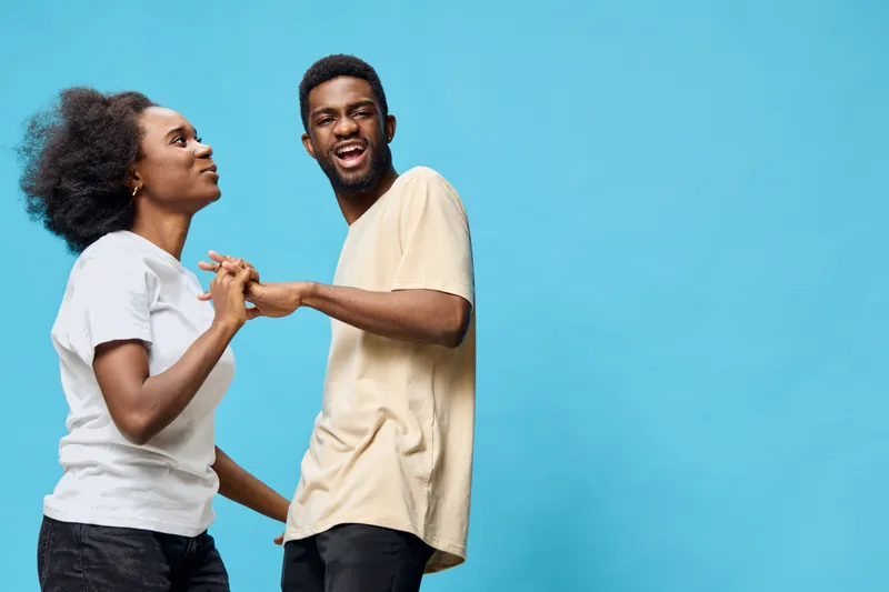 Two cheerful models dancing together on a blue background, showcasing joy and connection through movement, perfect for lifestyle and social concepts