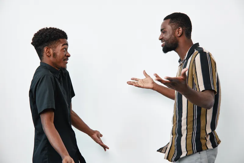 Two african american men with dark skin having a lively conversation in casual clothes on white background. Young black males expressing emotions and gestures in studio.