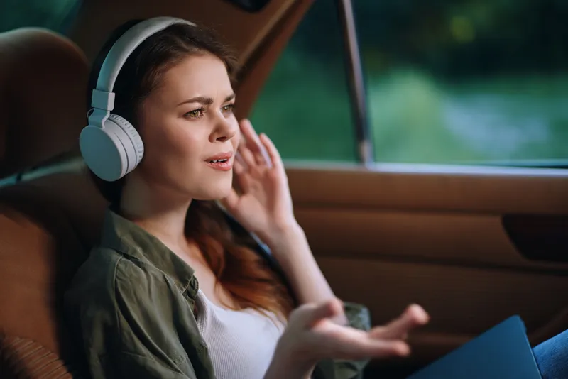 Young woman listening to music with headphones, expressing emotions while sitting in a car, cozy atmosphere, travel concept, relaxed mood, natural colors.