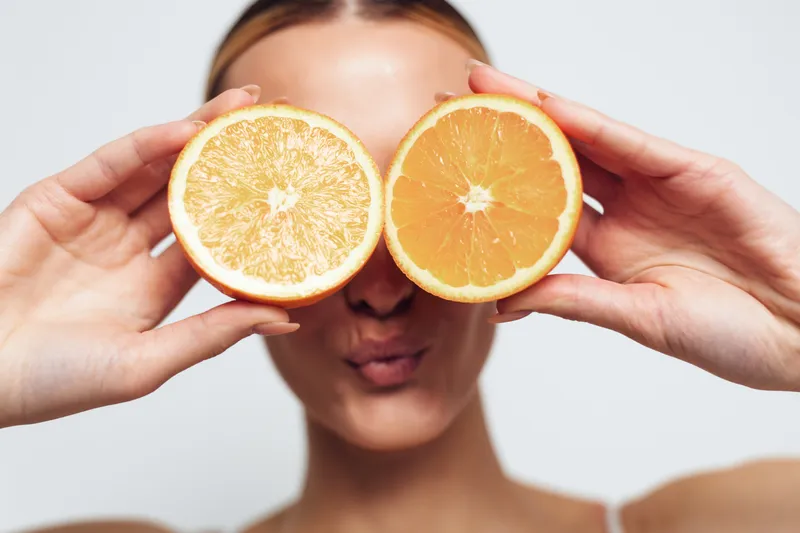 Woman holding citrus orange and grapefruit halves over eyes, blurred face, close up hands on foreground, vitamin C wellness concept, healthy lifestyle and freshness, diet, nutrition