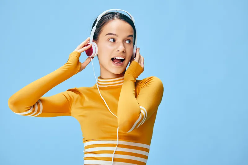 Woman in vibrant fitness vibe wearing a yellow athletic top, listening to headphones against a blue backdrop. Activewear scene celebrating sport, energy, music and motivation.