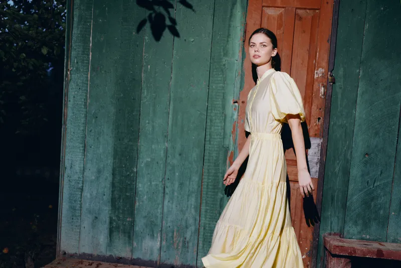 woman portrait fashion dress walking by wooden door in sunlight vintage photography with authenticity inclusivity casual pose