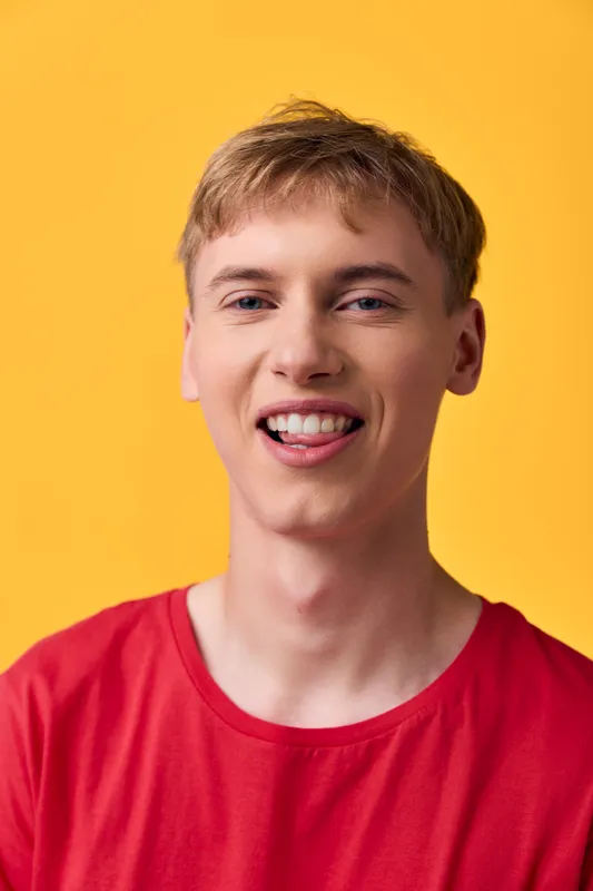 Smiling young man in a red shirt against a bright yellow backdrop, showcasing a friendly, approachable vibe suitable for lifestyle, fashion, or youth campaigns