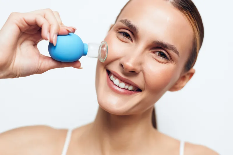 Smiling woman takes hydration water from a blue cup held by hand, promoting health, oral wellness and treatment, closeup face of adult on clean white background, care today