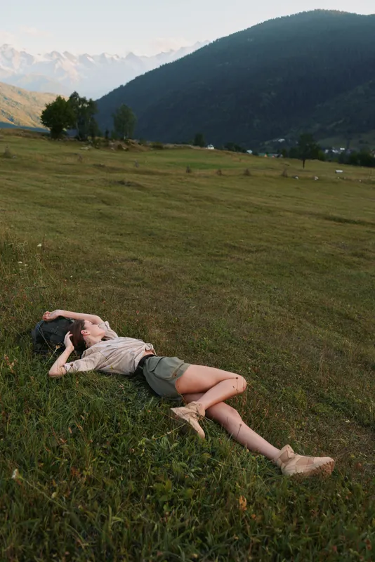 Young woman lies on green grass in mountain meadow relaxes enjoys nature outdoors casual lifestyle summer day peaceful environment fresh air