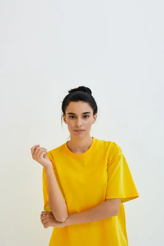 young woman wearing bright yellow t-shirt standing against white background with calm expression, casual style, minimalistic composition, natural lighting