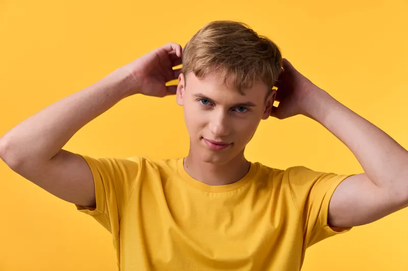Headphones on ears, a youthful male in a yellow shirt against a vivid backdrop, capturing a casual listening moment with modern style for lifestyle and music stock