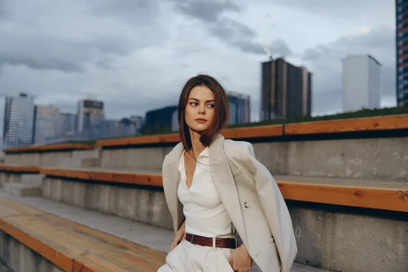Confident businesswoman in modern city setting, dressed in stylish white attire, exuding professionalism and elegance against an urban backdrop.