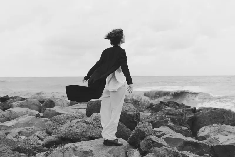 Business travel on rugged rocks along the ocean, wind sweeping hair, a silhouette with briefcase toward the horizon in monochrome tones
