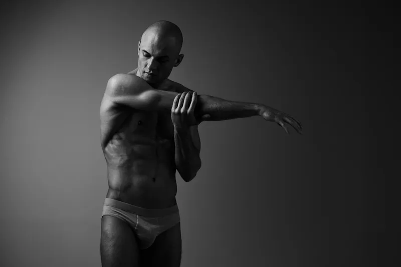 Athletic man posing in black and white, showcasing strength and grace. The powerful composition highlights his muscles and form elegantly.