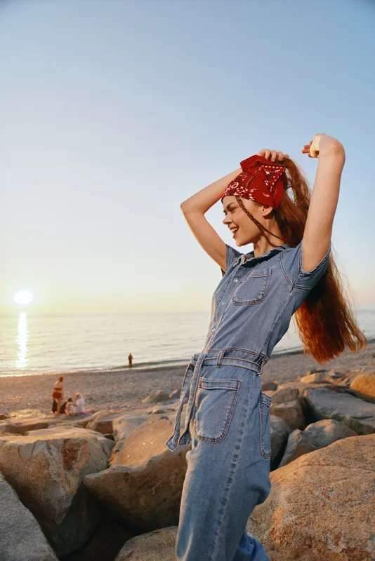 lifestyle woman in modern boho-western denim street style enjoys sunny beach sunset with film color warmth and relaxed joyful vibe outdoors