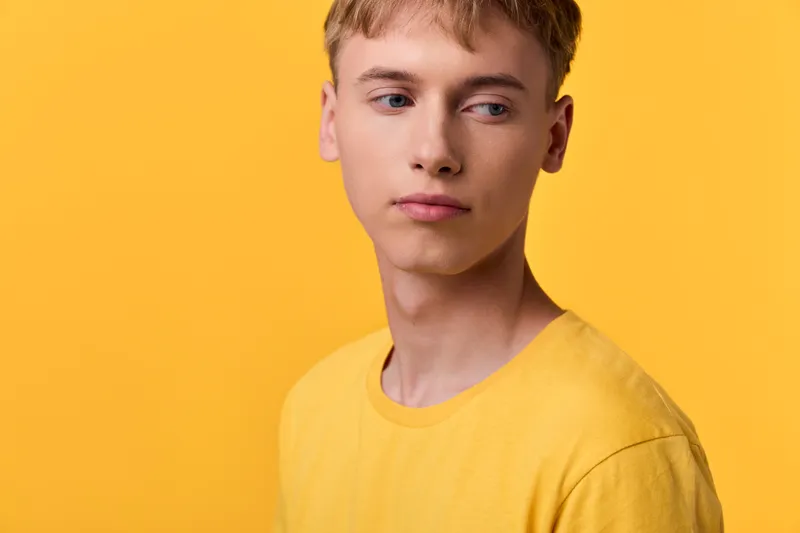 Youthful man against a yellow background in casual attire in a studio setting, exhibiting a thoughtful expression for fashion photography with clean image and soft lighting.