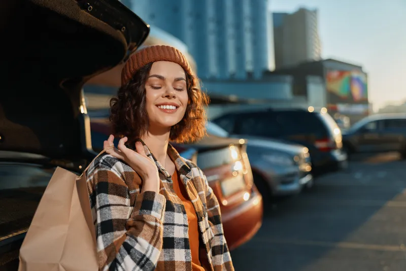 woman shopping car parking smile urban scene of a young woman with shopping bag by open trunk in golden hour glow, candid lifestyle mood, authenticity, mindful living and emotional storytelling