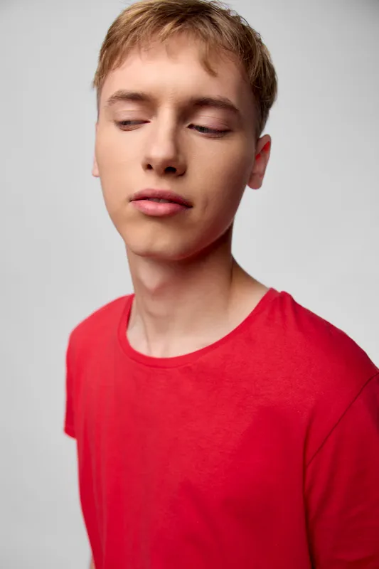 Young man in a red shirt with a calm expression and closed eyes, studio shot with neutral background, head and shoulders composition, minimalism, thoughtful mood and soft lighting