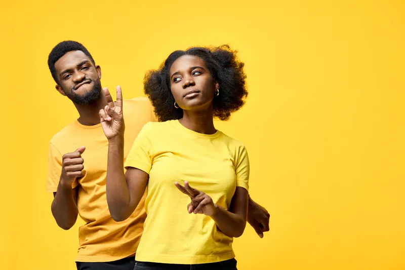 Energetic young couple dancing joyfully against a vibrant yellow background, showcasing playful expressions and matching casual attire in a lively setting