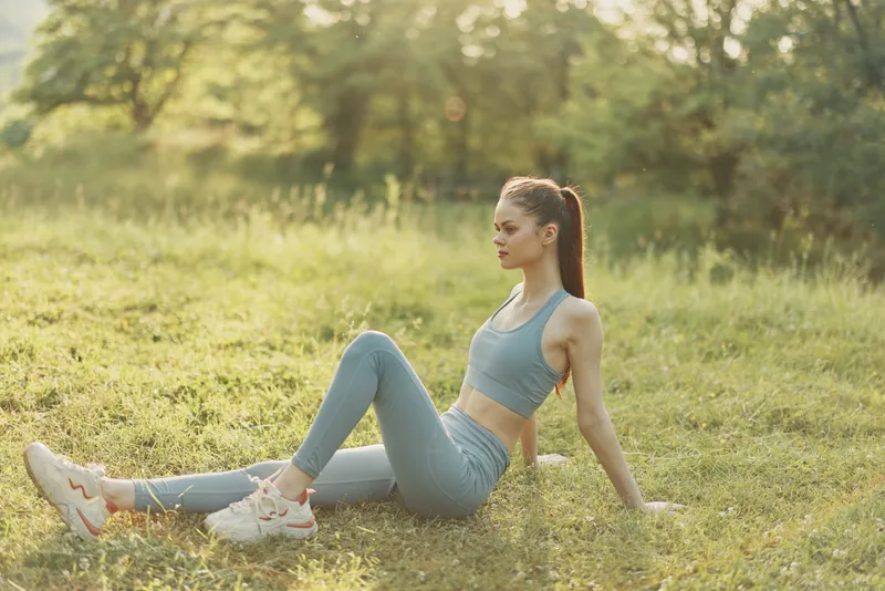 Fit young woman relaxing in a green field, wearing sportswear, enjoying nature and the warm sunlight, highlighting a healthy lifestyle and fitness journey