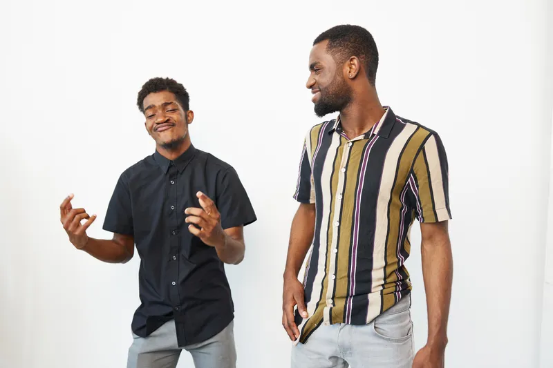 Two cheerful African American men enjoying a moment together, dressed in stylish outfits, expressing joy and friendship in a bright indoor setting.