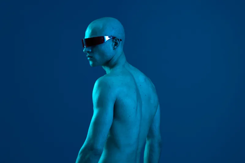 Strong man with sunglasses, showcasing a blue light backdrop, emphasizes confidence and modernity in a striking way. Unique black and white aesthetic enhances depth.