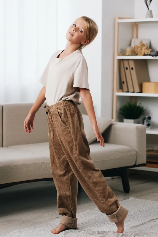 Authentic lifestyle shot of a girl at home, embodying a playful school vibe with casual attire and a relaxed, candid pose in a cozy living room, under natural light, inviting everyday routine.