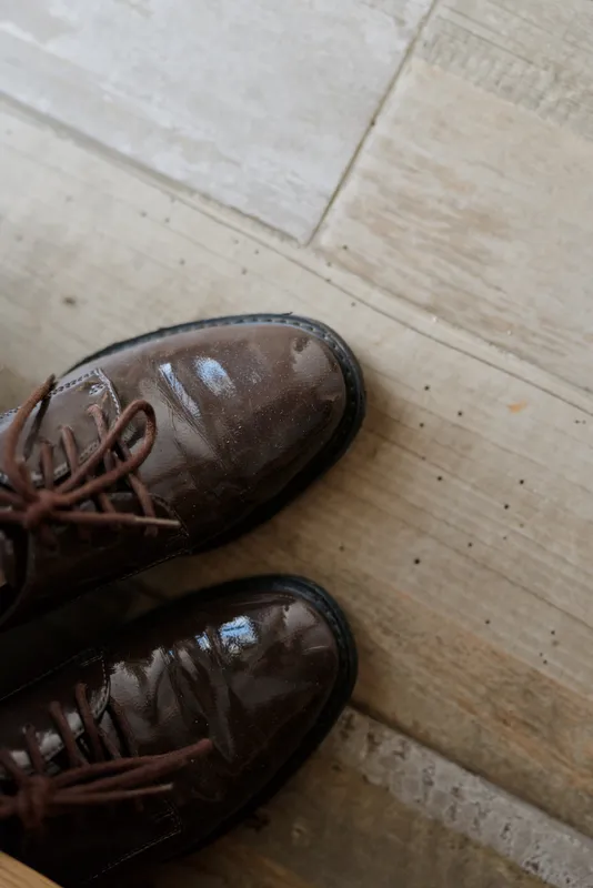 A pair of brown polished leather shoes sit on a wooden floor in a cozy home setting, suggesting everyday routine, attention to detail, practical style, and a calm, organized lifestyle.