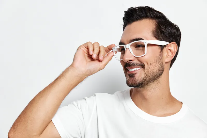Smiling man wearing white glasses and casual white t-shirt, looking at the camera with a friendly expression, isolated on plain solid background. Lifestyle concept.