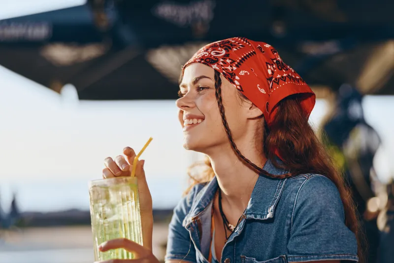 lifestyle woman with denim jacket sipping a drink outdoors in modern boho-western street style, film color vibe, smiling and relaxed in natural light