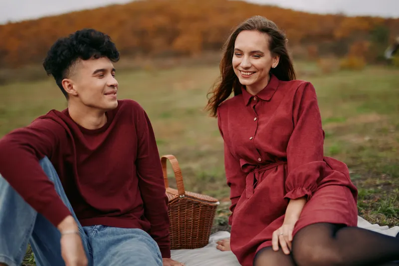 A candid outdoor picnic portrait of a young couple in an autumn meadow, showing authentic connection and genuine expressions, natural poses and a trustworthy atmosphere highlighting real relationship