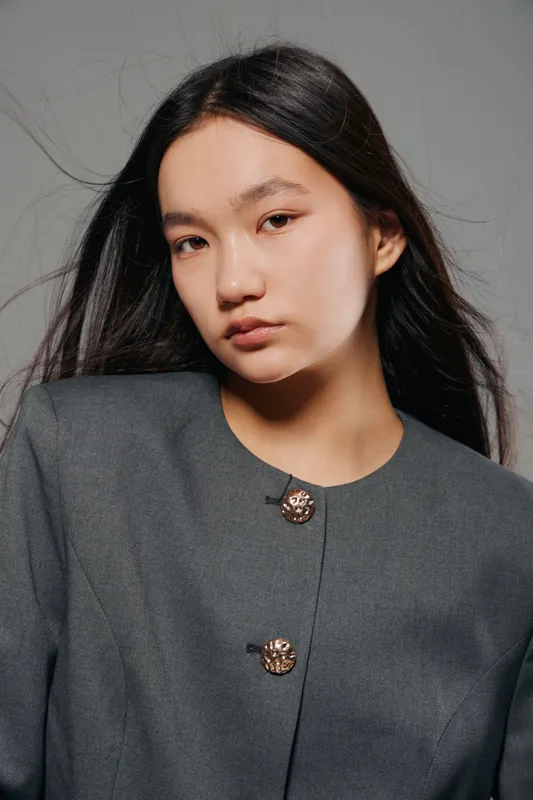 Young woman portrait with long dark hair in fashionable grey coat posing against neutral background for beauty, style, fashion and confident expression with soft lighting
