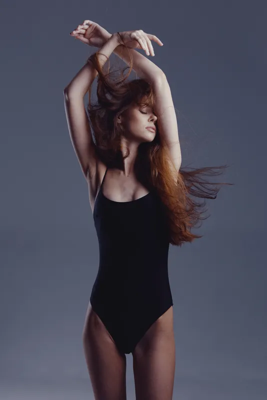 graceful woman dancing in black bodysuit with flowing hair against grey background