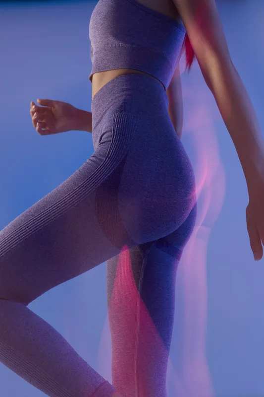 Woman sport fitness wearing seamless purple activewear, showing dynamic motion and strength in modern gym lighting with a smooth blue and pink background.